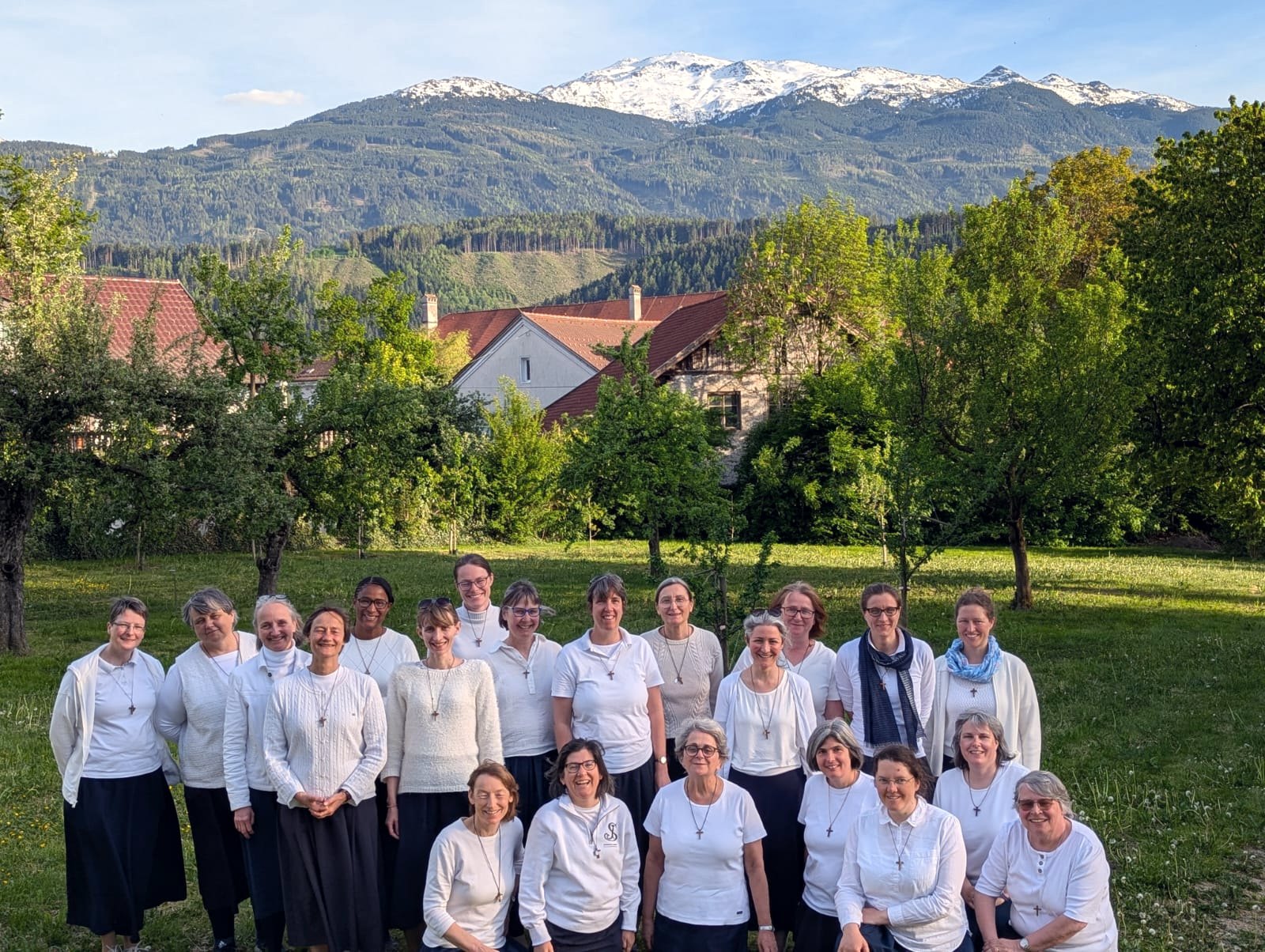 Gruppenfoto gottgeweihter Schwestern der Gemeinschaft Emmanuel in weißen Oberteilen auf einer Wiese, im Hintergrund verschneite Berge